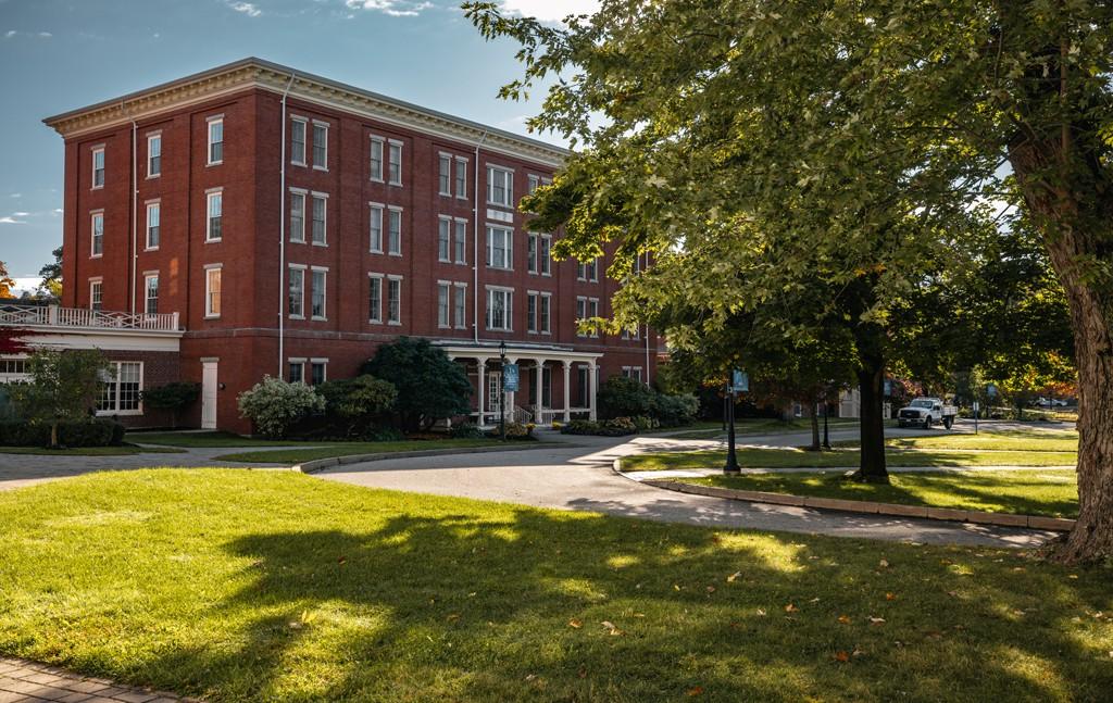 A brick building sits behind green grass and a large tree